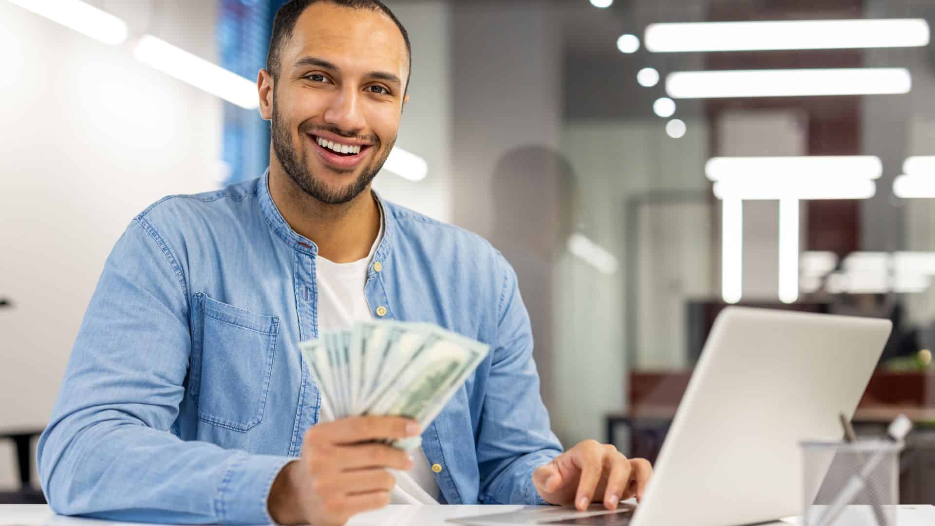 Man holding cash sitting at his desk.