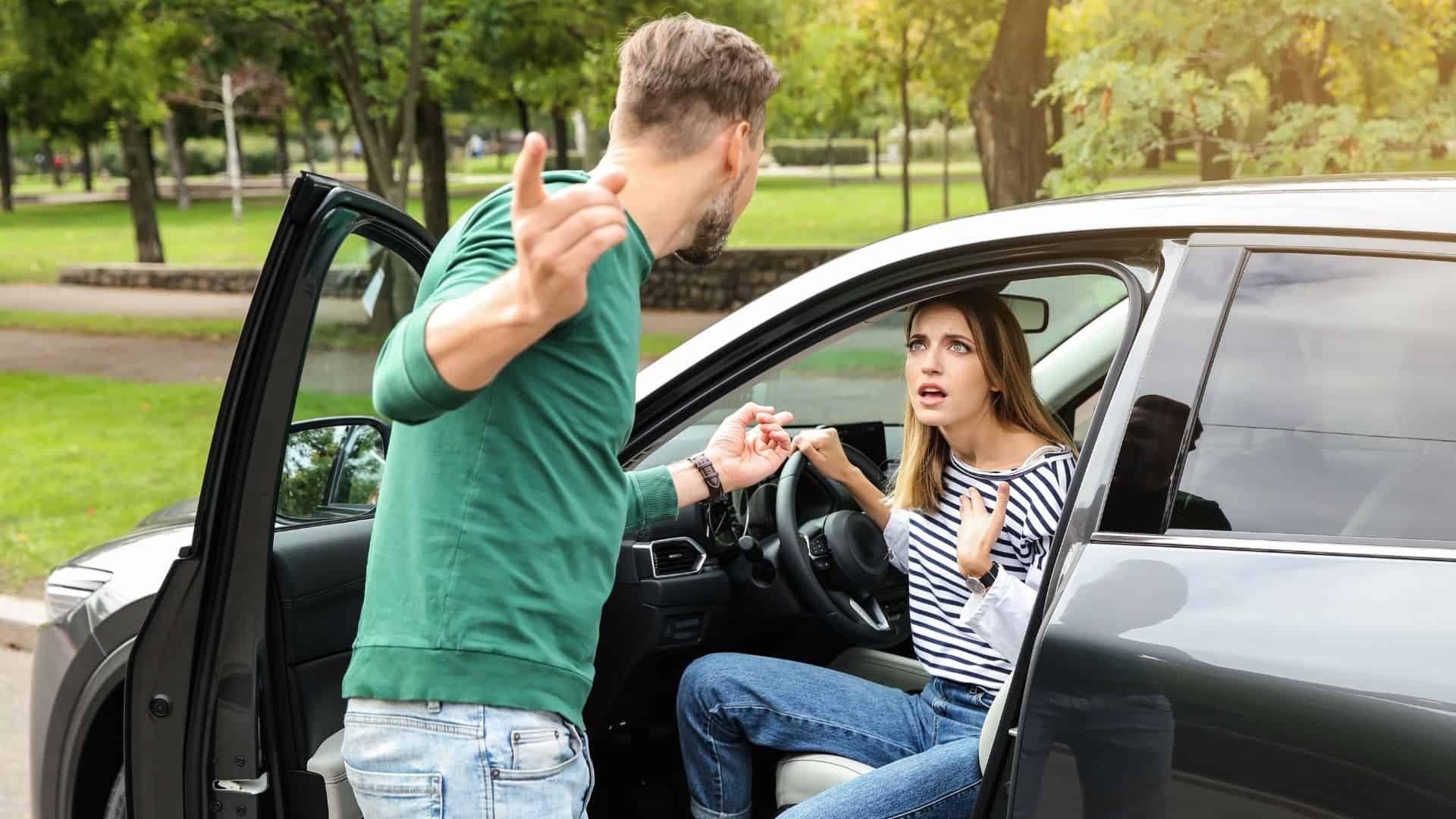 Man arguing with woman who is sitting in a car.