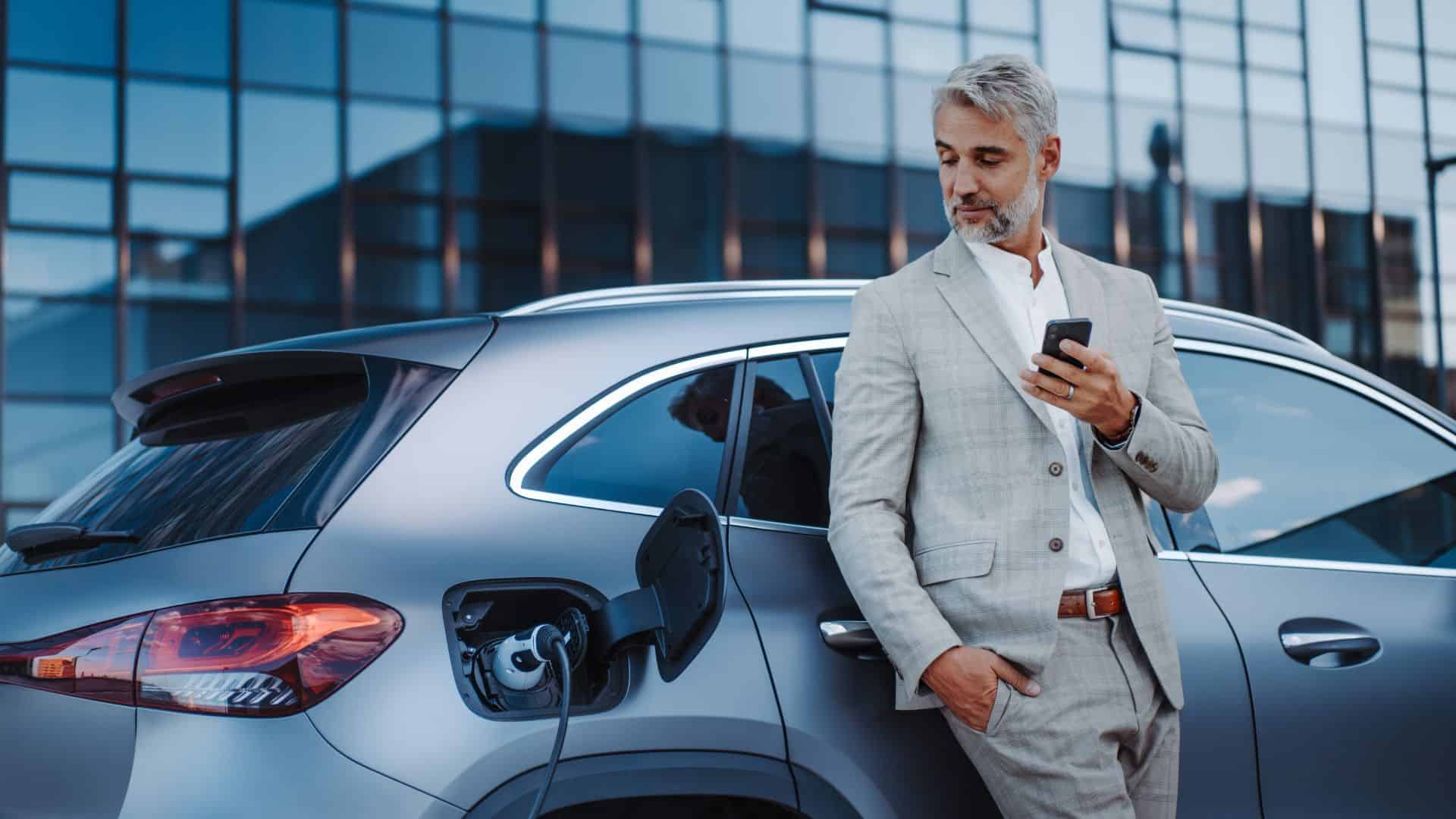 businessman holding smarphone looking at his EV charging