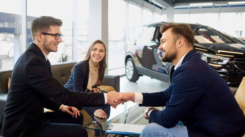 Professional men shaking hands at car dealership, car sales, business meeting, confident, modern showroom. 