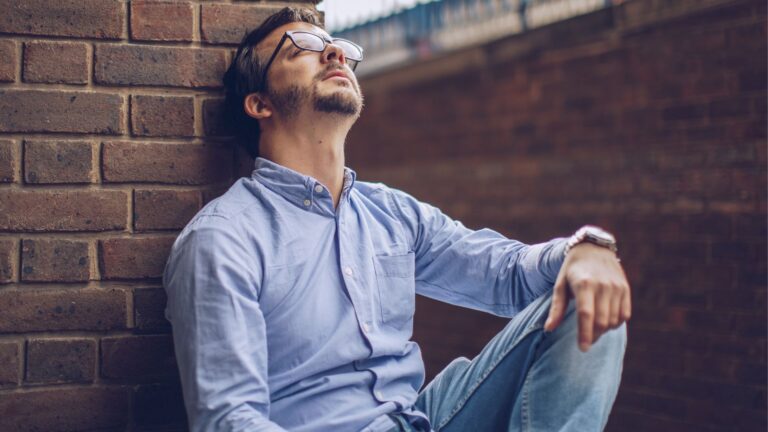 Relaxed man leaning against brick wall, stylish casual fashion for men's lifestyle.