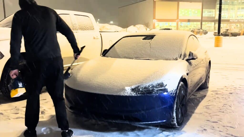 Snow-covered luxury sports car during winter night, being cleaned at parking lot.