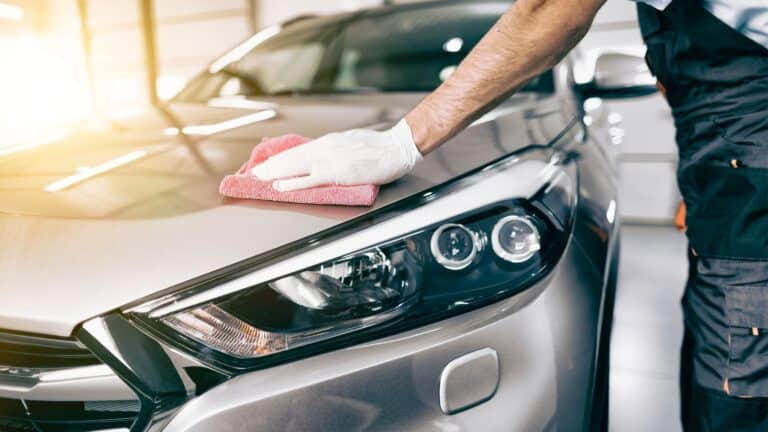 Man holding a red rag, wearing gloves, detailing the hood of his car