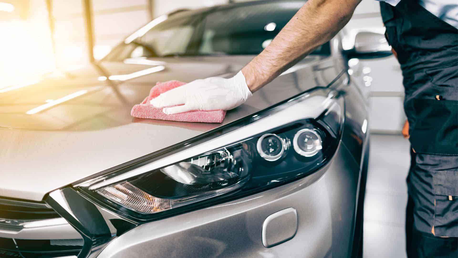 Man holding a red rag, wearing gloves, detailing the hood of his car