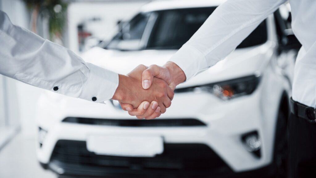 Two people shake hands as they make a deal over a used car