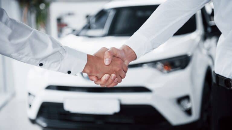 Two people shake hands as they make a deal over a used car