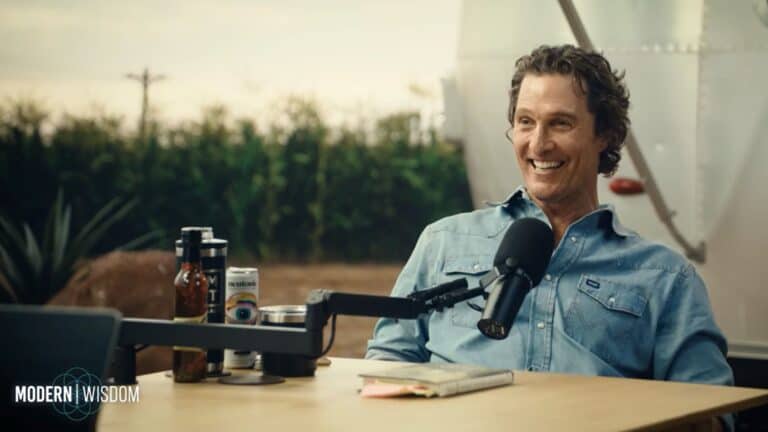 Matthew McConaughey smiling, sitting in front of a microphone on the set of the podcast Modern Wisdom