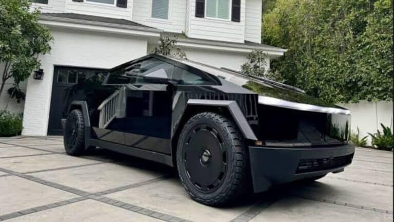 Futuristic black Tesla Cybertruck parked in driveway with modern house in background.