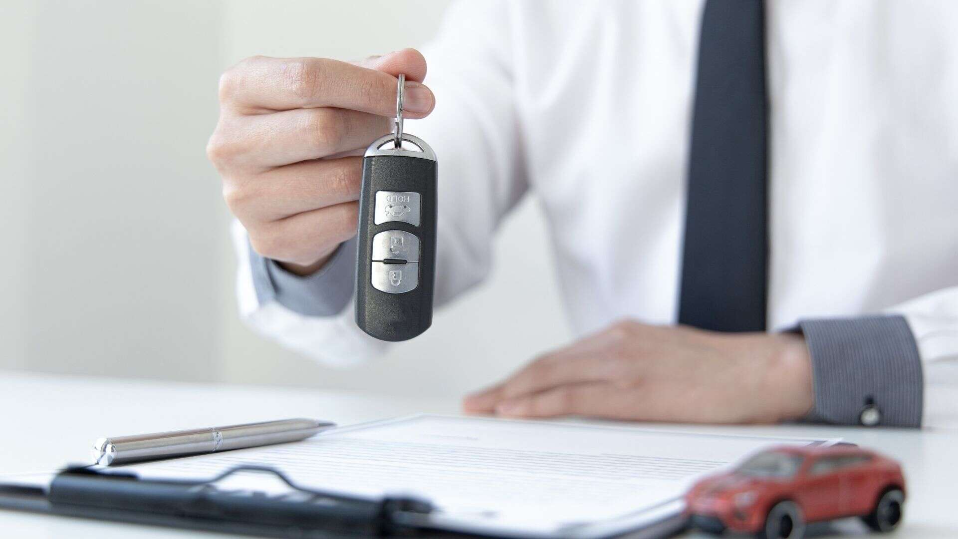 Car salesman sitting at desk with contract, ready to hand over car keys