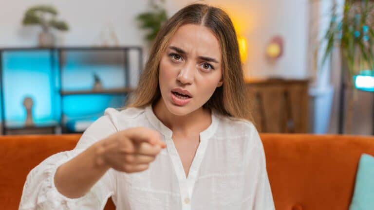 woman sitting on sofa couch at home, angrily pointing