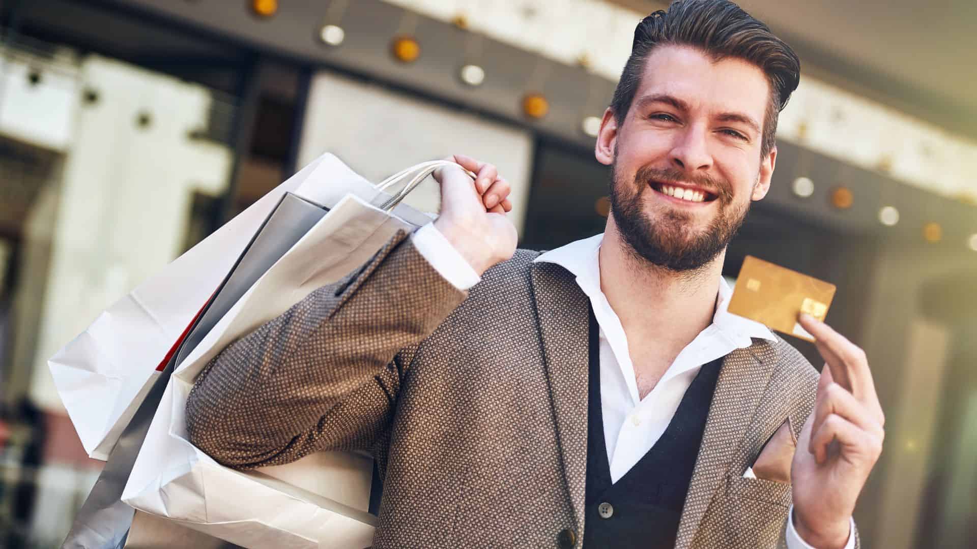 man holding credit card in one hand, and shopping bags in other