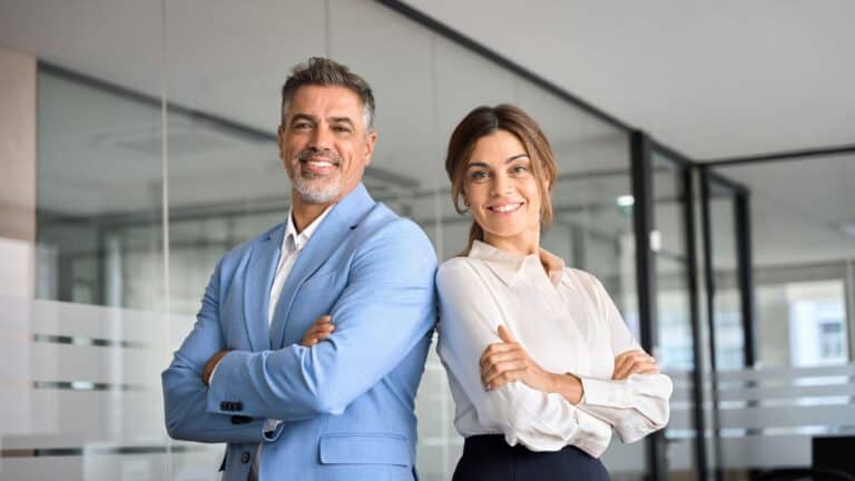 businessman and woman standing arms crossed in office at work looking at camera