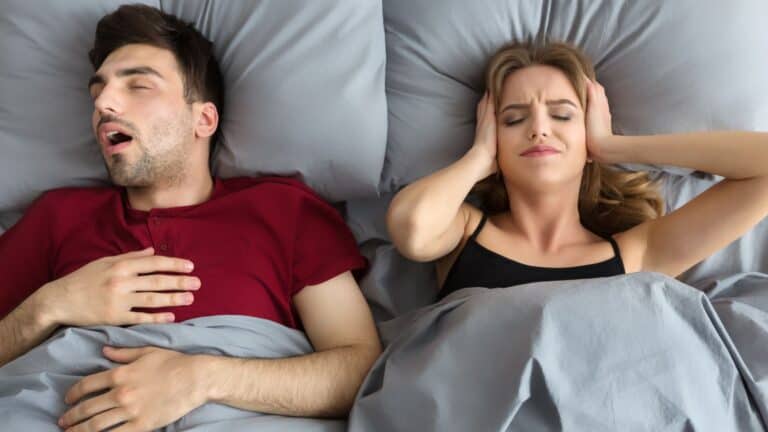 A man snoring loudly next to annoyed wife