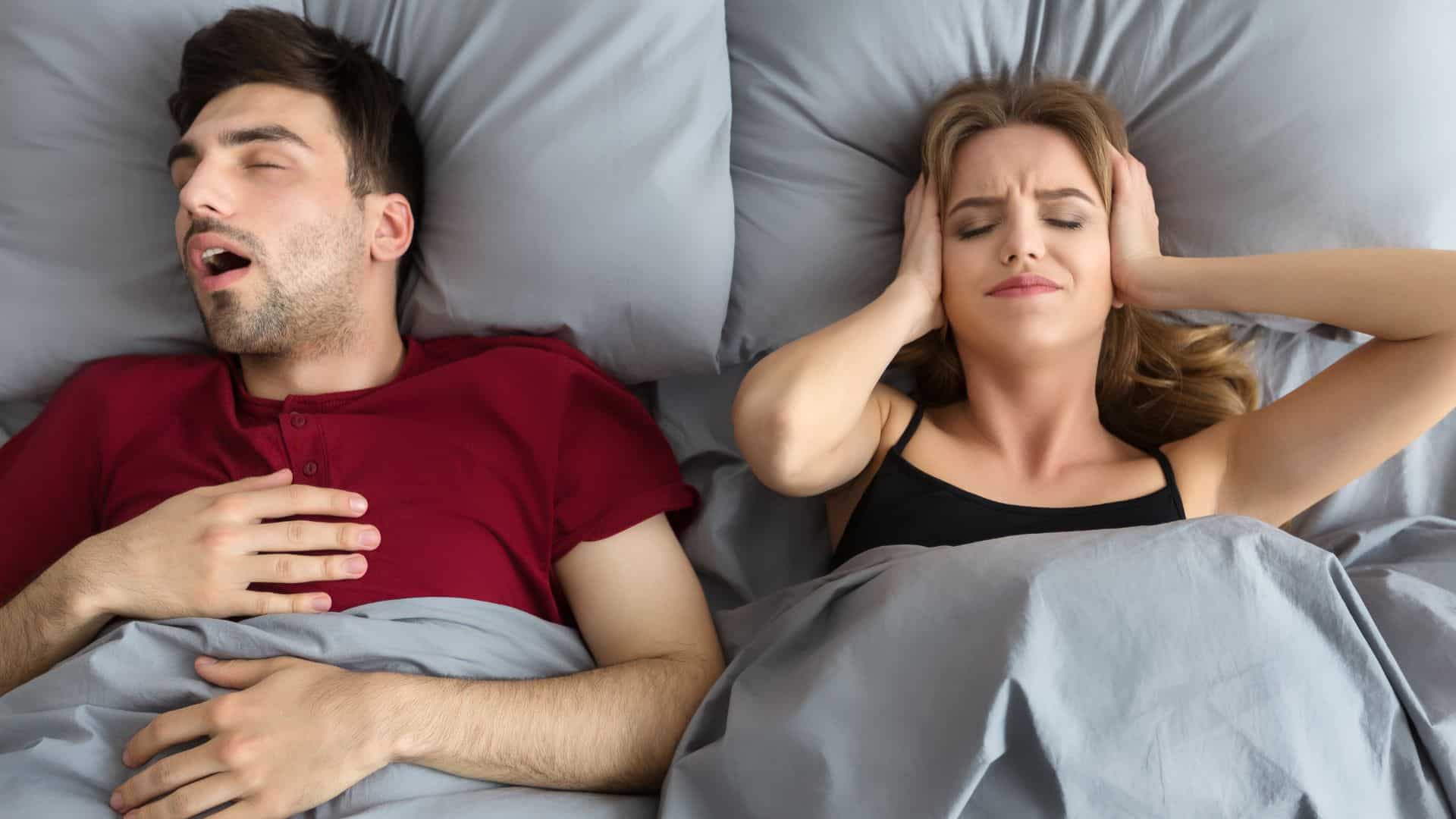 A man snoring loudly next to annoyed wife
