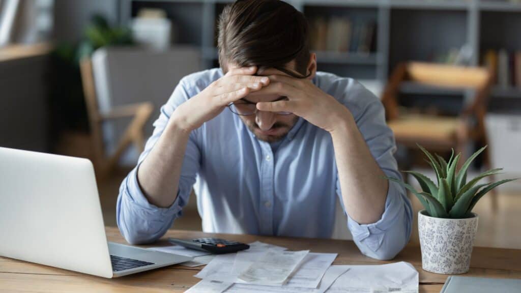 Stressed man grab head in despair checking finance documents