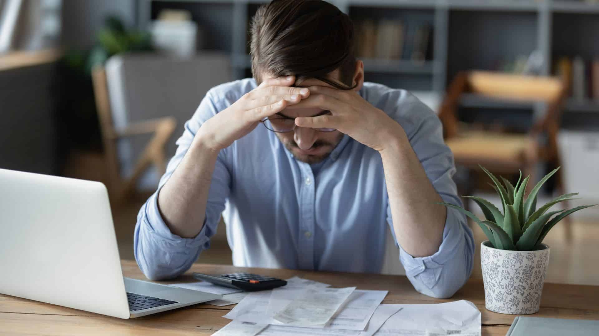 Stressed man grab head in despair checking finance documents