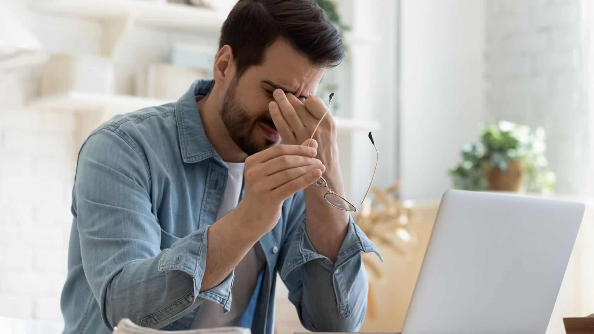 Tired man sitting at desk rubbing his eyes