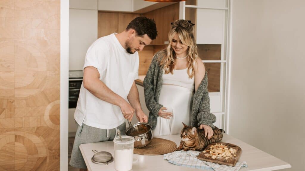A man in the kitchen baking with his pregnant wife