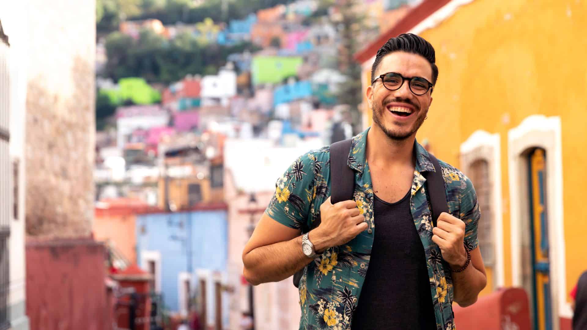 Smiling man with backpack exploring colorful urban neighborhood.