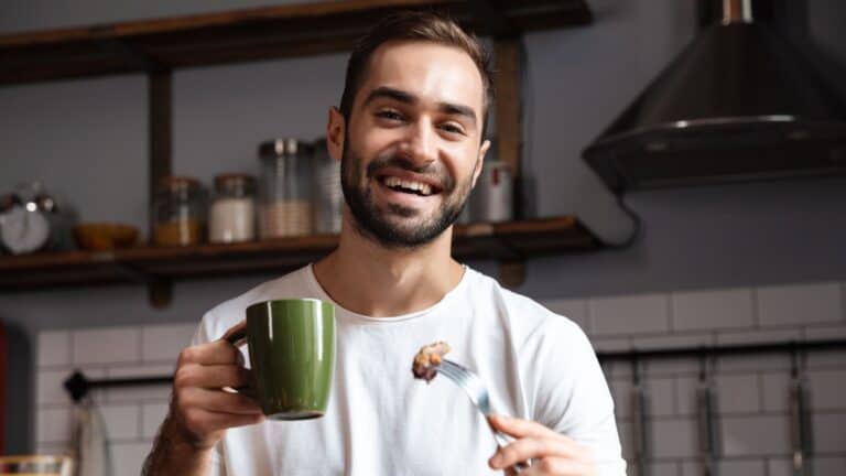 A man holding a cup of coffee getting ready to eat a bite of food