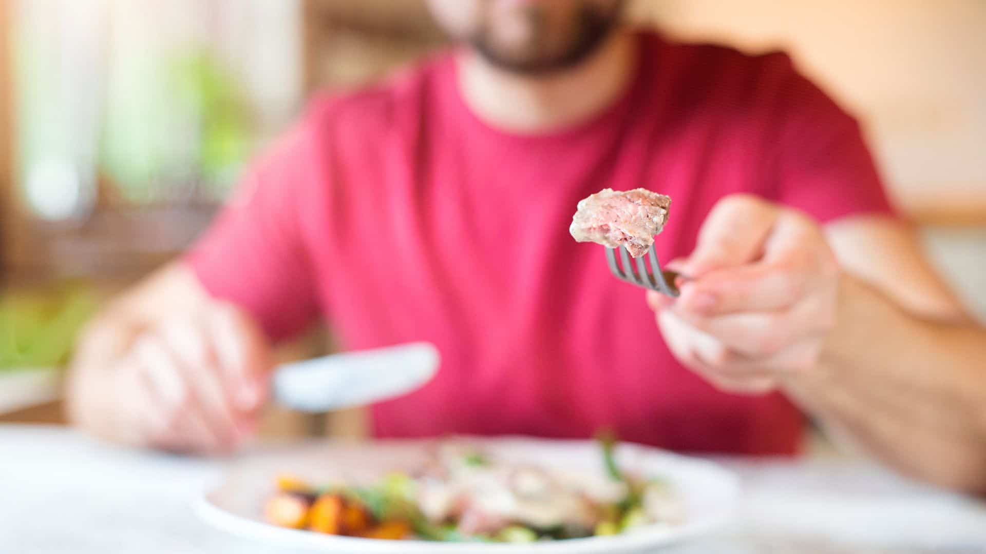 Man eating dinner holding a piece of steak on a fork