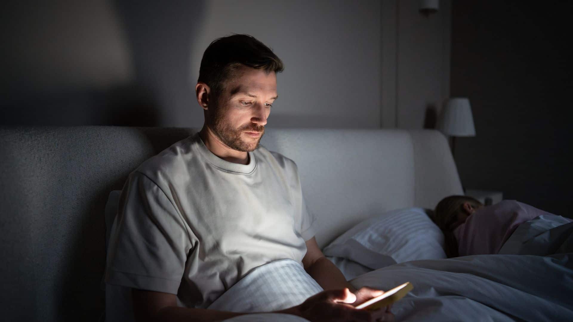 A man sitting up in his bed looking at his phone