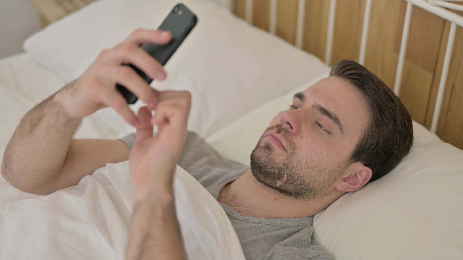 A man laying down in bed holding his phone an scrolling
