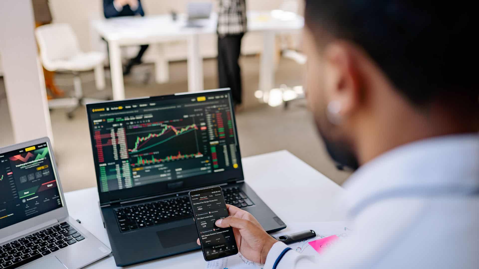 Person using his cellphone with stock market opened on his laptop in background