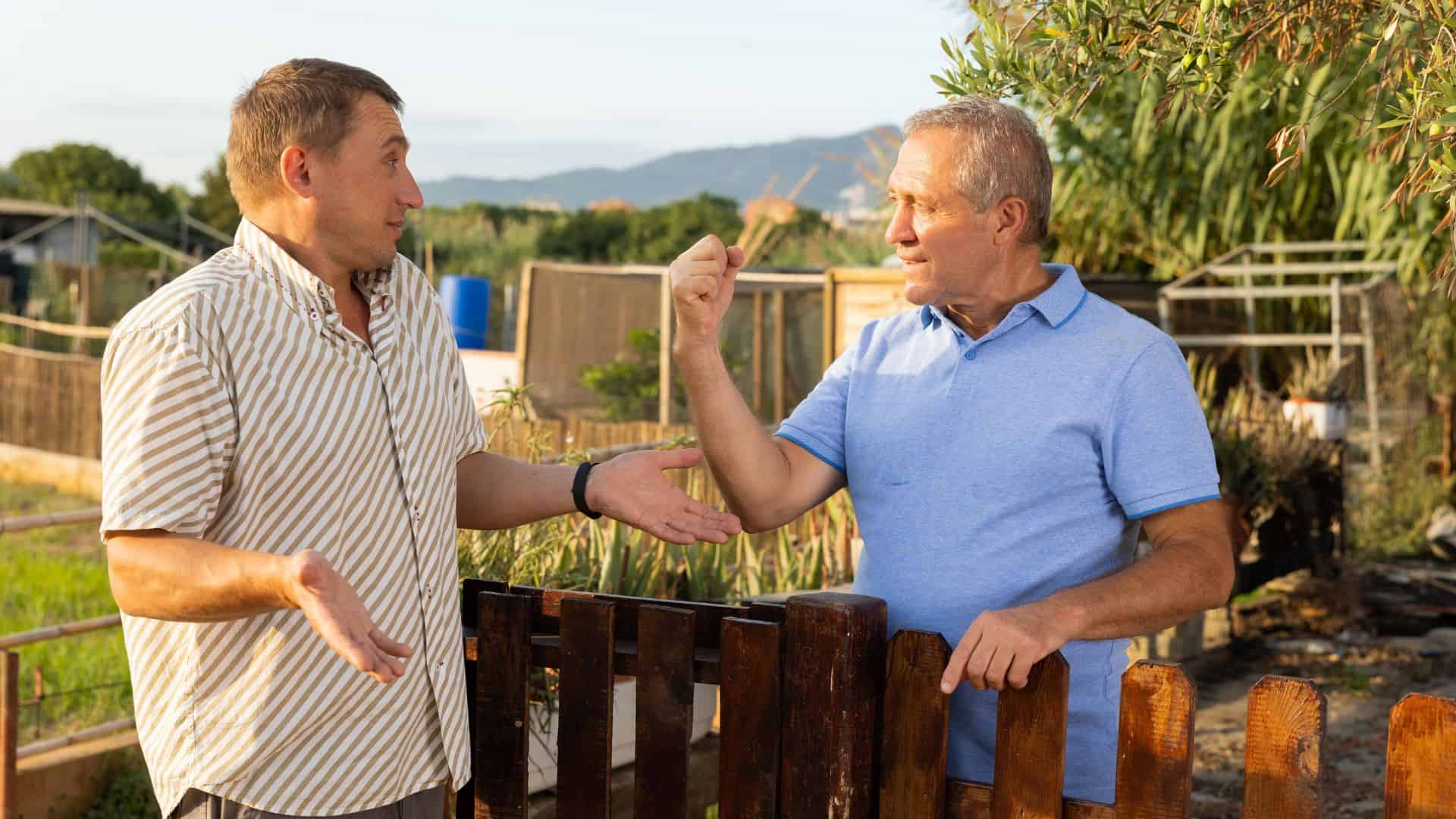 Two men neighbors standing at fence of backyard