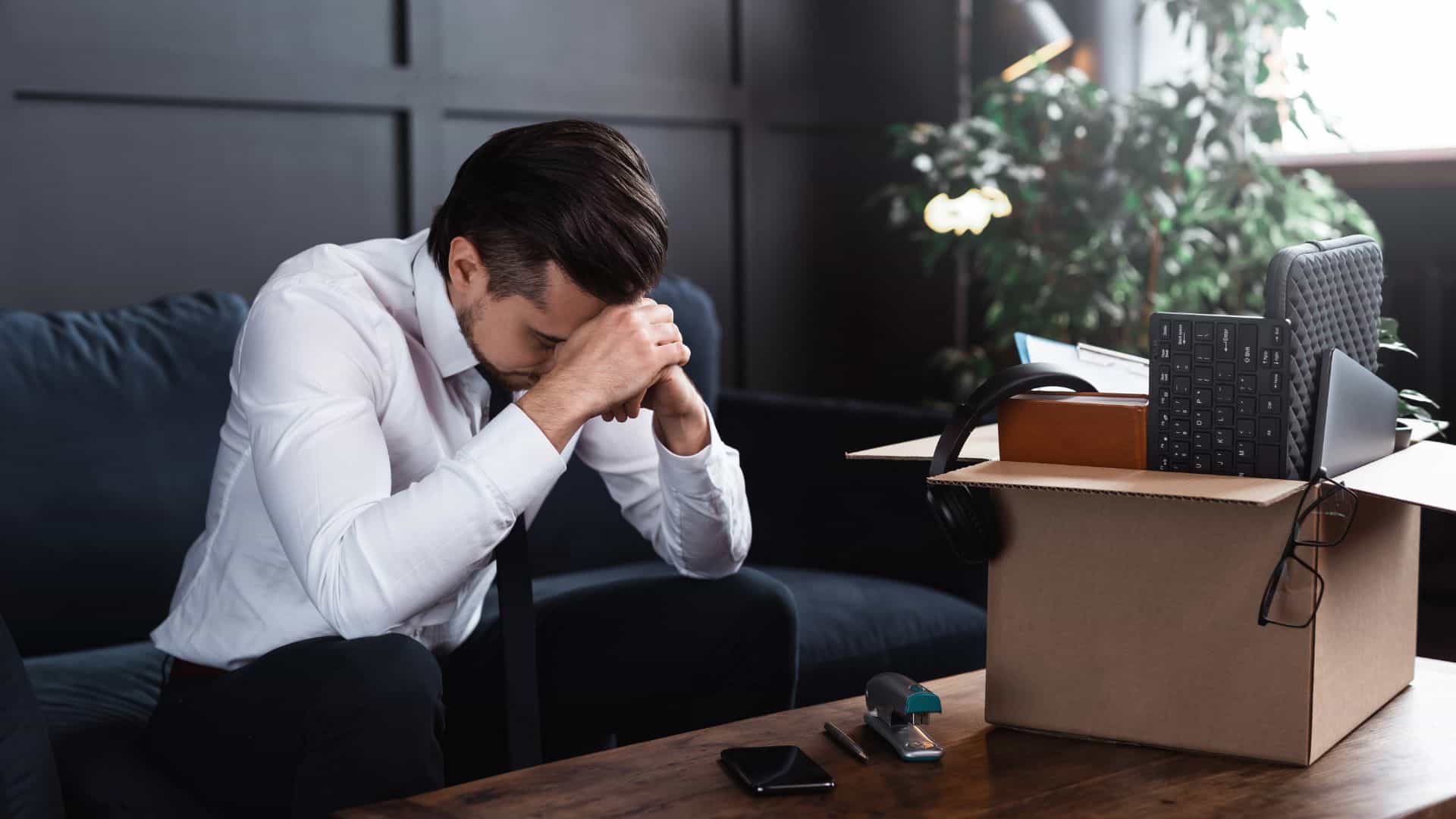 A young man is sitting, stressed, with a box of his belongings on the table.