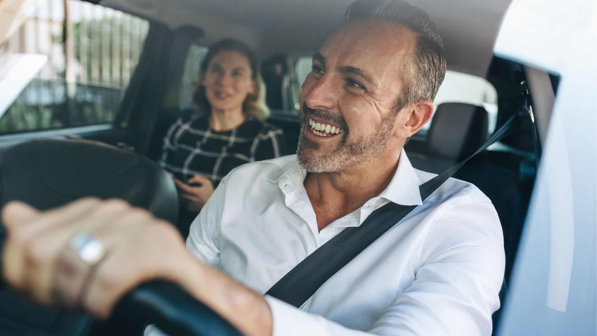 A man is test driving a car with a woman in the back seat