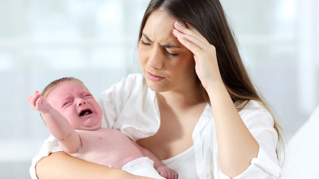 Desperate mother holding her angry baby crying.